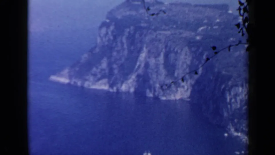 1960 coastal view near Rome with a rocky headland, blue sea, and visible 8mm frame edges.