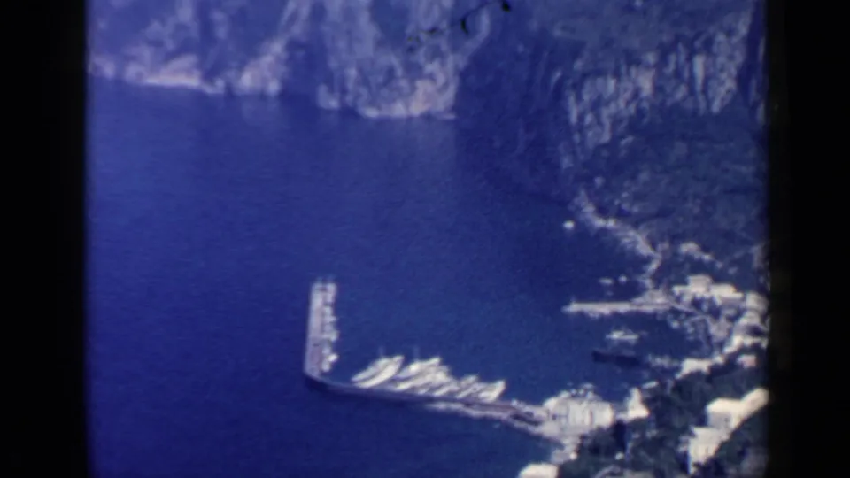 Wide 1960 Rome-area coastal harbor view with boats, a long pier, cliff walls, and bright shoreline buildings.