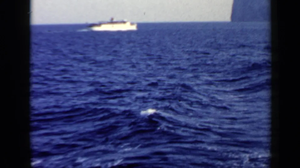 1960 8mm Rome-area ocean view with a distant boat above dark blue water and a breaking whitecap in the foreground.