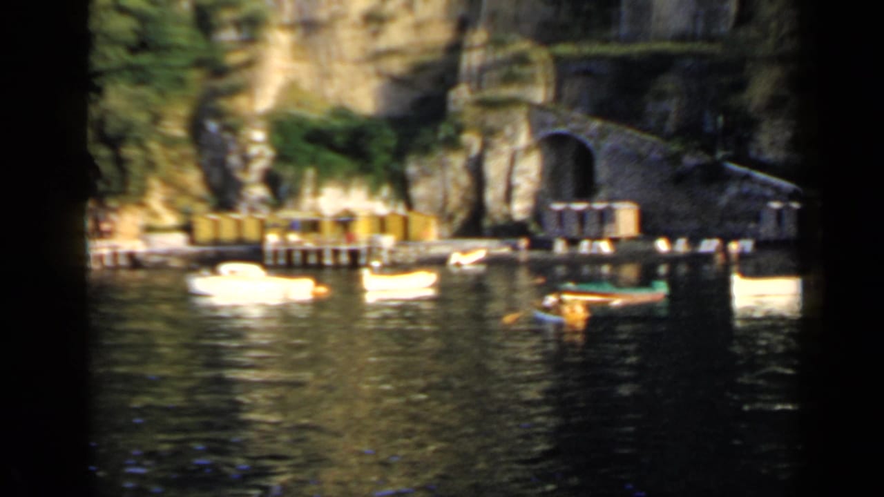 Small boats on calm water near a rocky cliff with an arched waterfront tunnel.