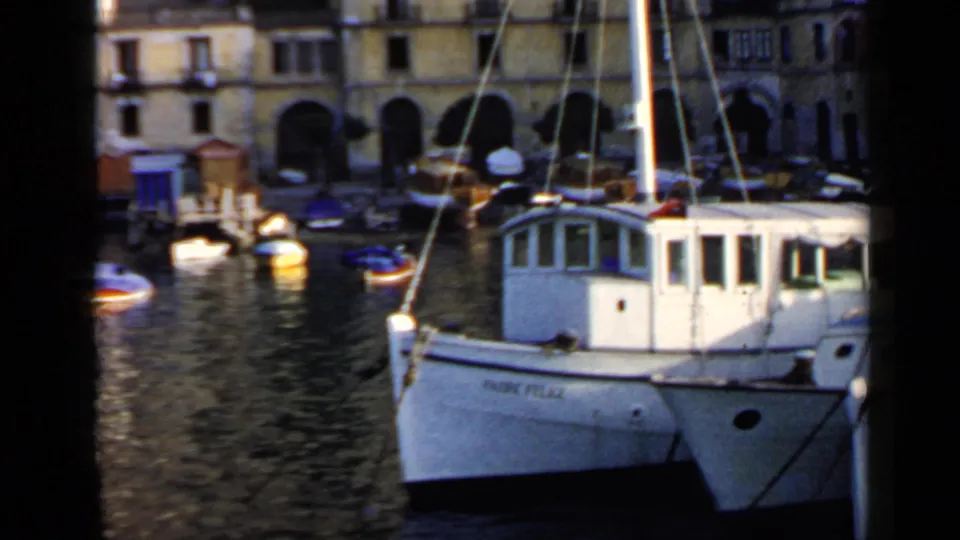 White vessel marked Fabio Felice moored in an Italian harbor with stone waterfront buildings and small boats behind it.