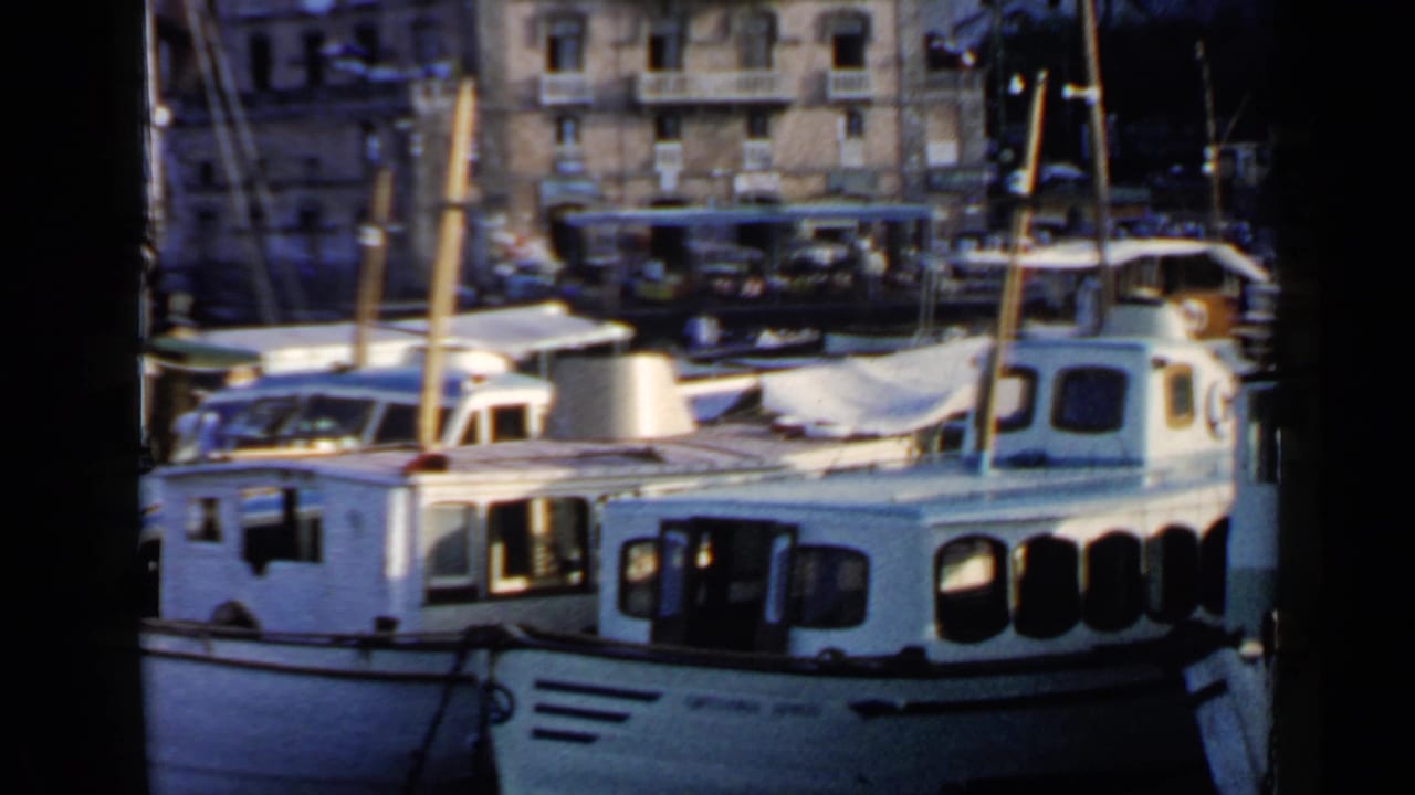 White moored boats with masts beside waterfront buildings and a bus in the background.