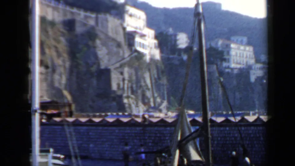The 1960 Rome, Italy footage looks toward cliffside houses above a seawall, with boat rigging and small people near the waterfront.