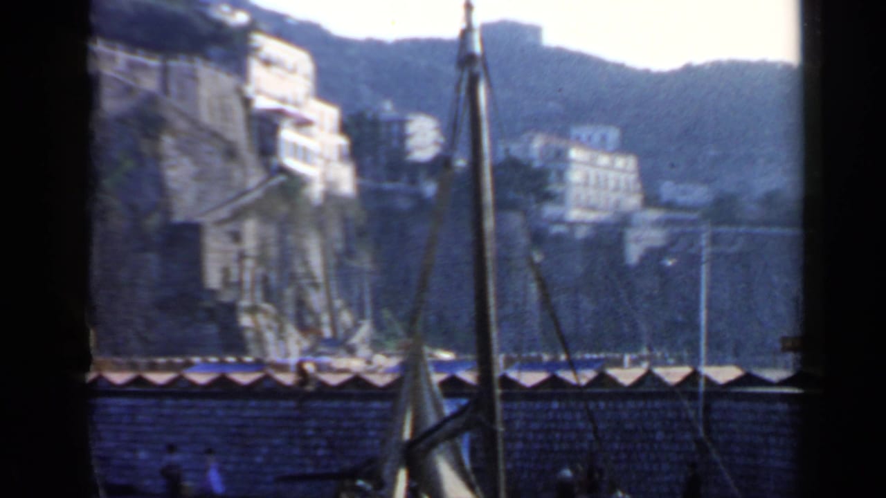 Harbor view with sailboat mast, hillside buildings, water, and dark film borders.