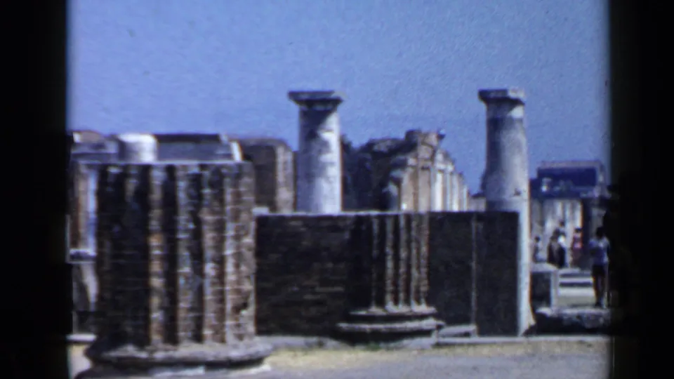 1960 8mm Rome travel frame showing stone ruins, standing columns, and distant promenade visitors.