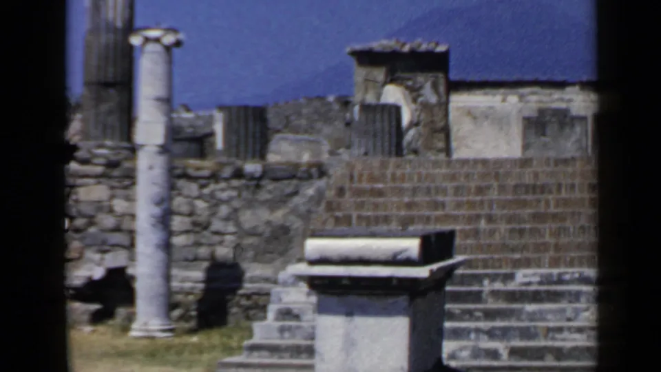 1960s 8mm view of Italian ruins with steps, a standing column, stone walls, a plinth, and sunlit masonry.