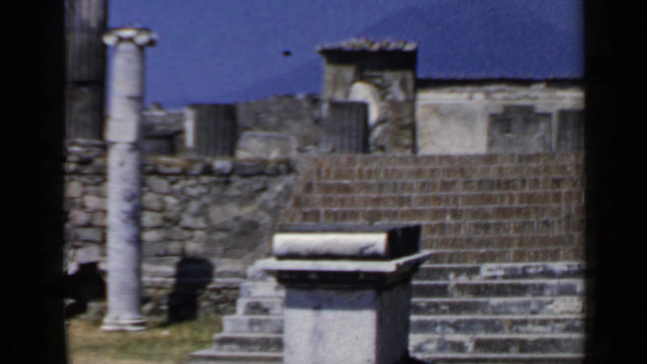 Stone steps, walls, columns, and a rectangular block under a blue sky.