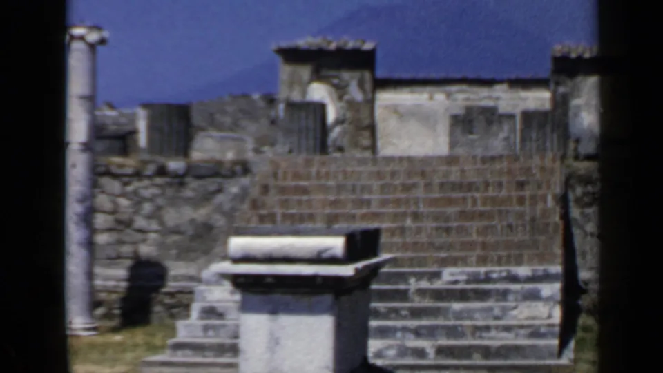 Rome travel footage frame from 1960 with broad stone steps, masonry, column pieces, and a pale rectangular block under clear sky.