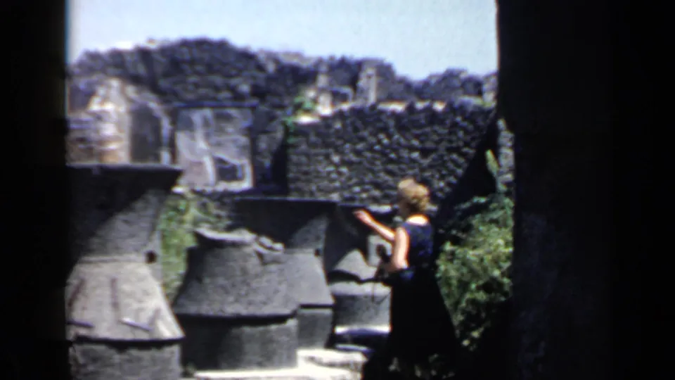 In the final frame, the woman appears to gesture beside weathered stone structures at the Italian ruins site.