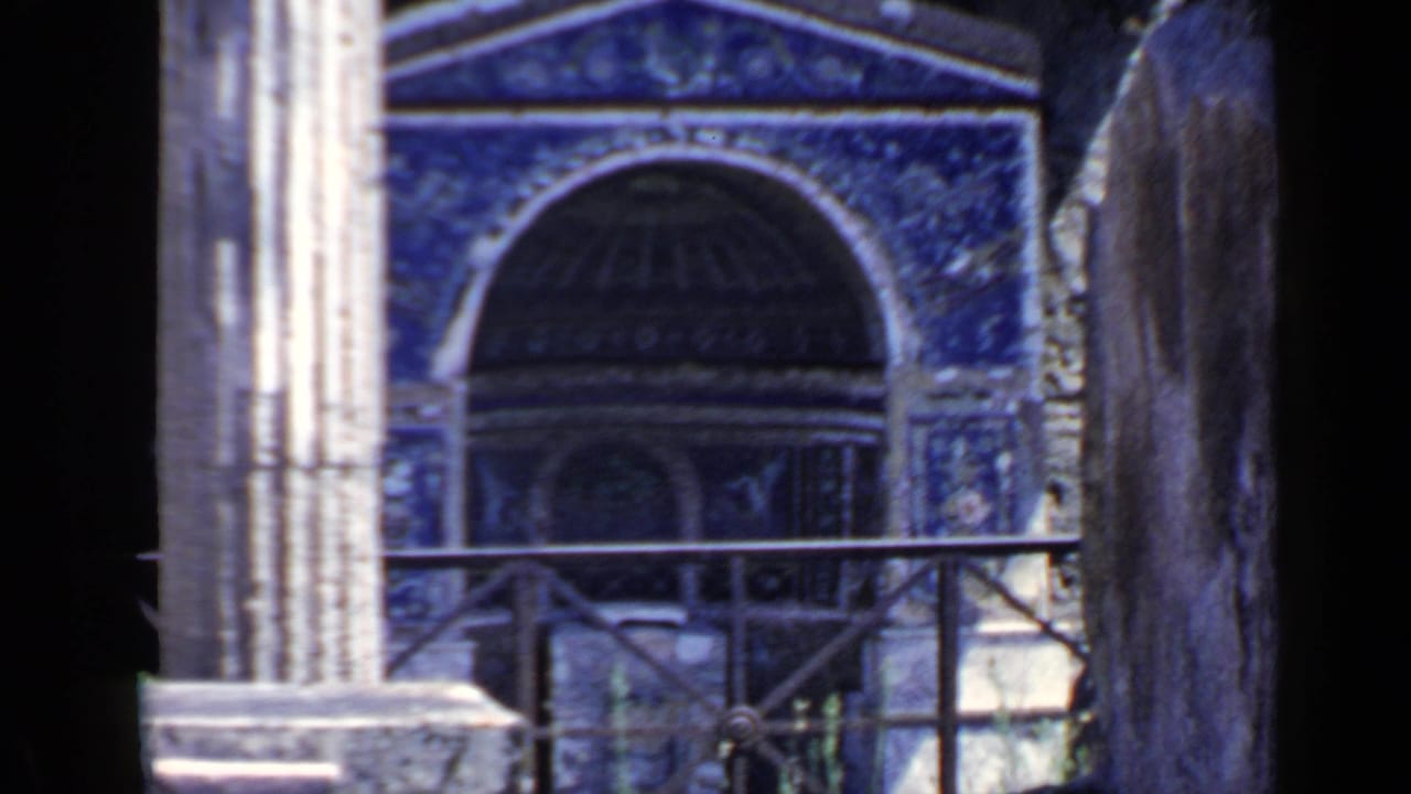 Blue mosaic archway framed by grey stone pillars with a metal railing in front.