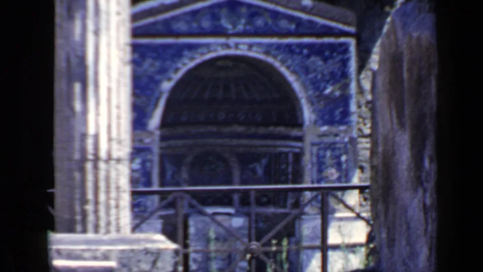 1960 Rome 8mm frame showing a blue mosaic archway, weathered grey pillar, dark opening, and foreground railing.