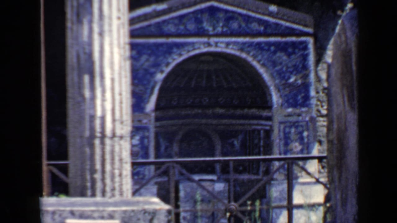 Mosaic archway and tall stone column viewed across a metal railing.