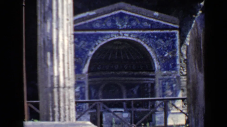 1960 Rome 8mm frame with a tighter view of the blue mosaic arch, grey pillar, dark interior, and foreground railing.