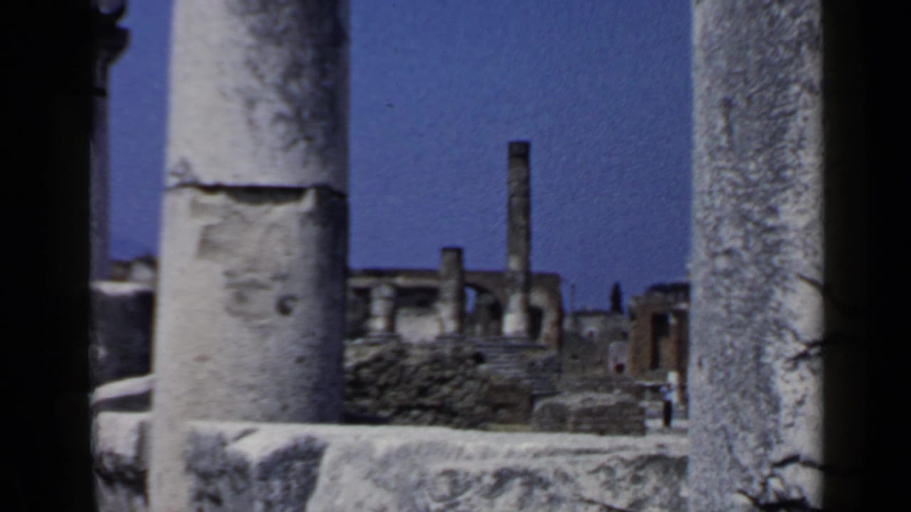 Stone columns frame distant ruins and visitors under a blue sky.