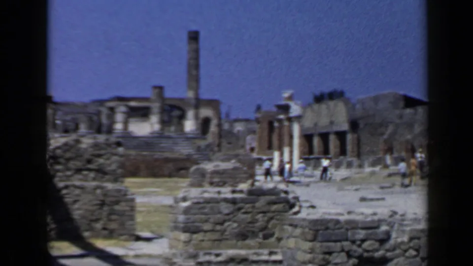 1960 8mm frame of Pompeii showing rough stone foundations, partial columns, and tourists near ruined structures.