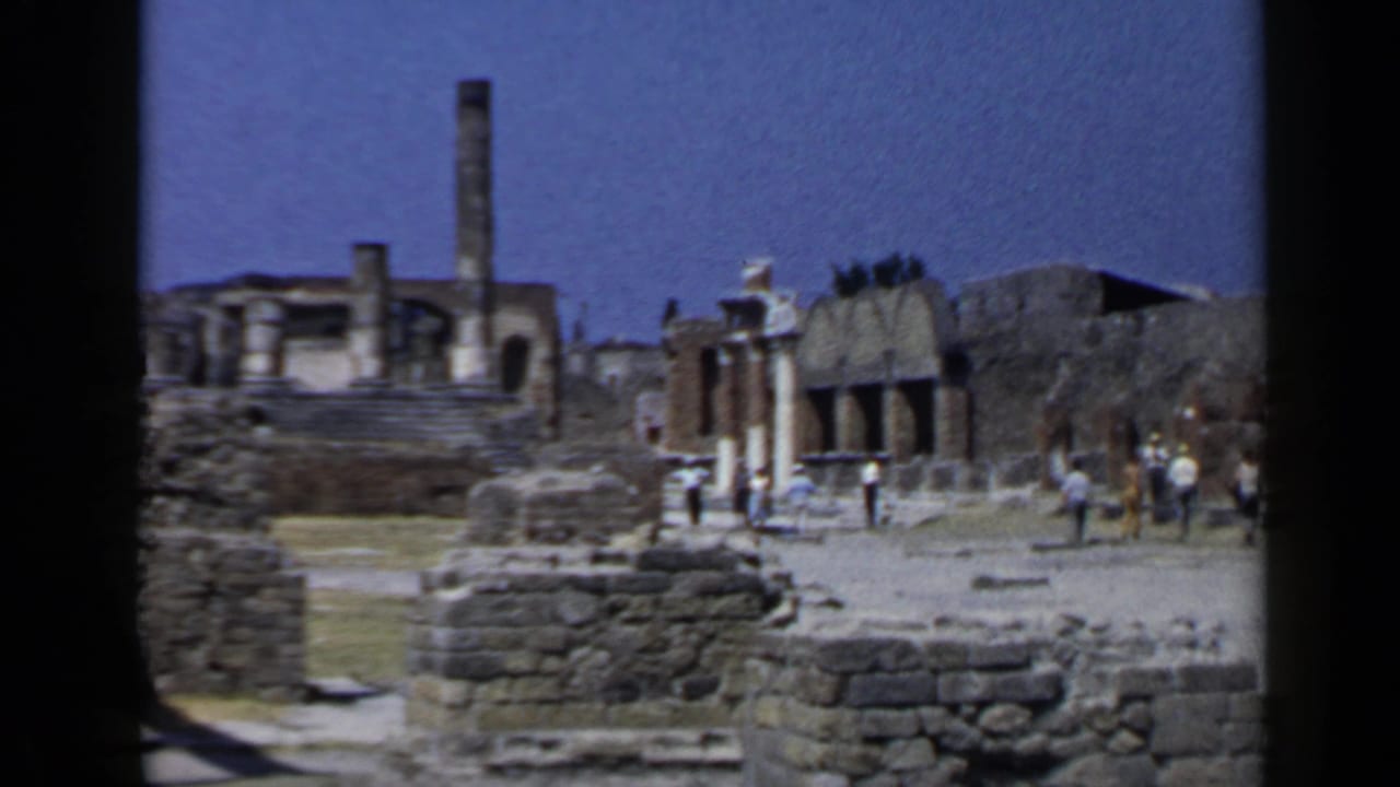 1960 Rome travel footage shows tourists moving through ancient stone ruins under a bright sky, with weathered walls and structures in view.