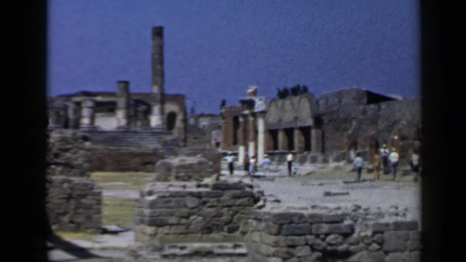 1960 Rome travel footage shows tourists moving through ancient stone ruins under a bright sky, with weathered walls and structures in view.