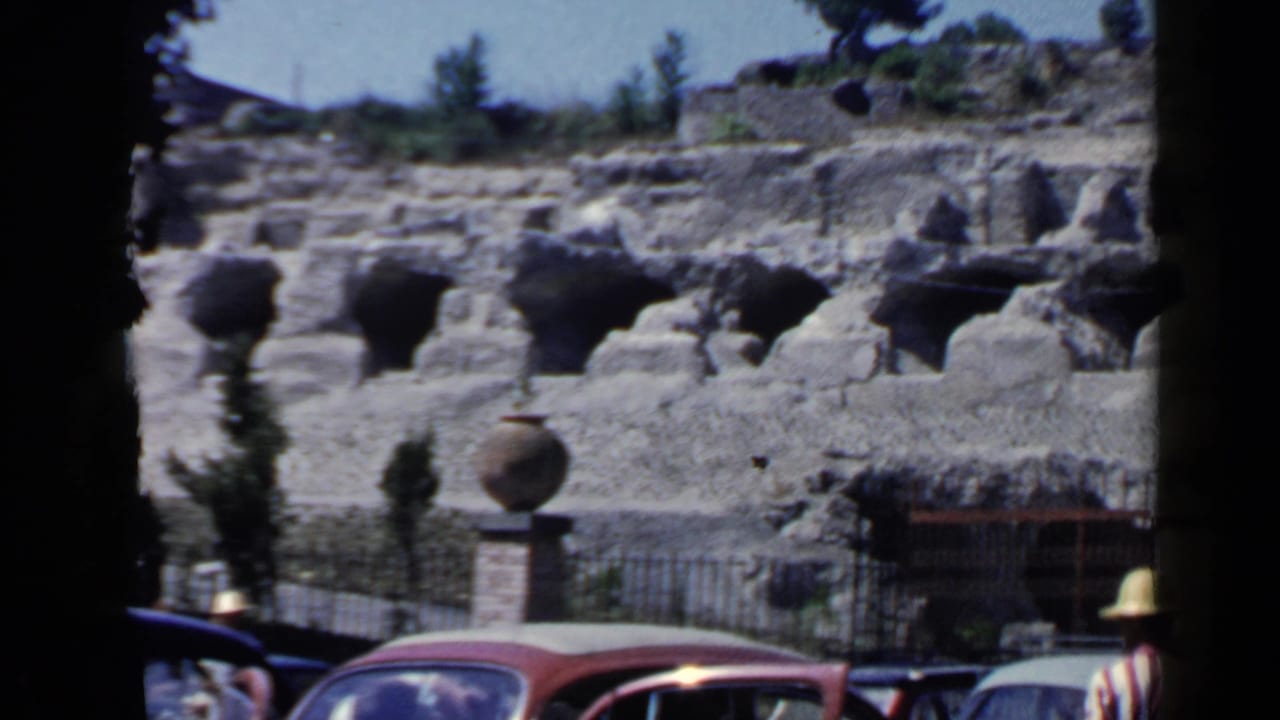 A Rome ruins scene shows arched stone recesses, fencing, pottery-like vessels, and parked mid-century cars along the visitor area.