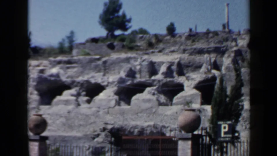 The closing frame shows Rome ruins with arched recesses above an iron fence, parked cars, large vessels, trees, and a visible parking sign.