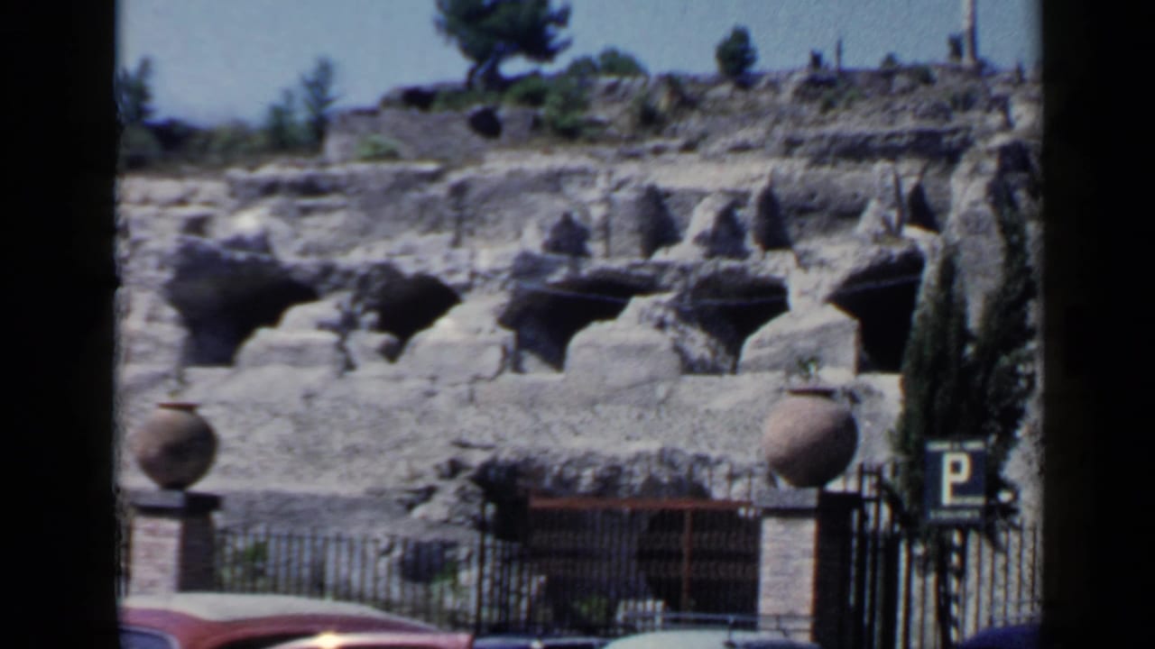 Stone ruin entrance with arches, parked car edge, gate, and parking sign.