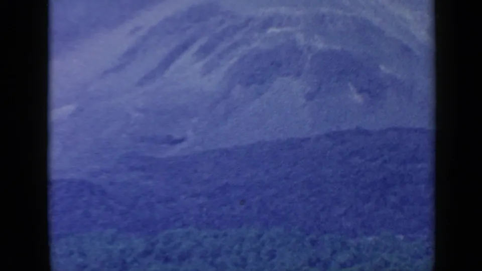 Soft 8mm view of a distant hazy mountain landscape, with blue sky and dark vertical film-frame borders.