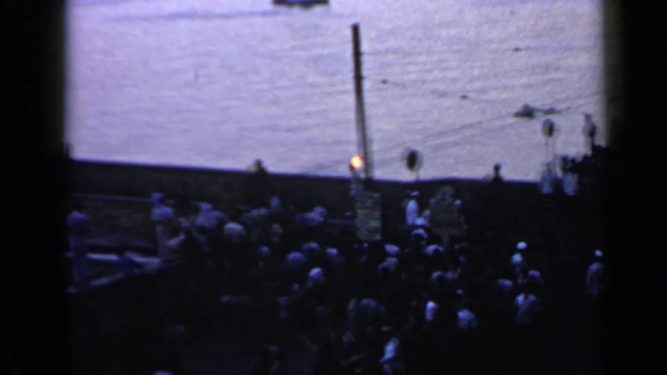 1960 Rome relay view with clustered spectators beside the water and the Olympic torch flame standing out in the dim light.