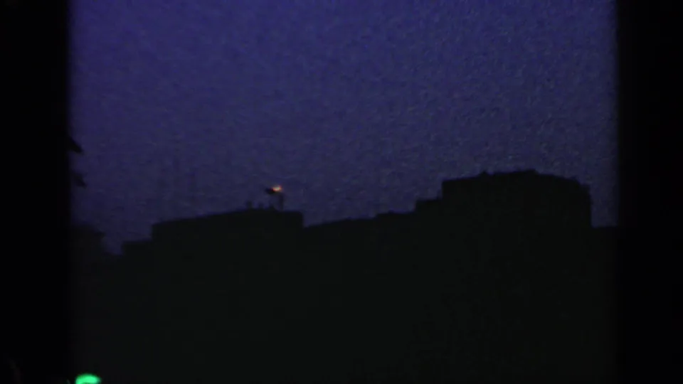 Distant 1960 Rome twilight frame with a small flame or light glowing above silhouetted riverside structures and water.