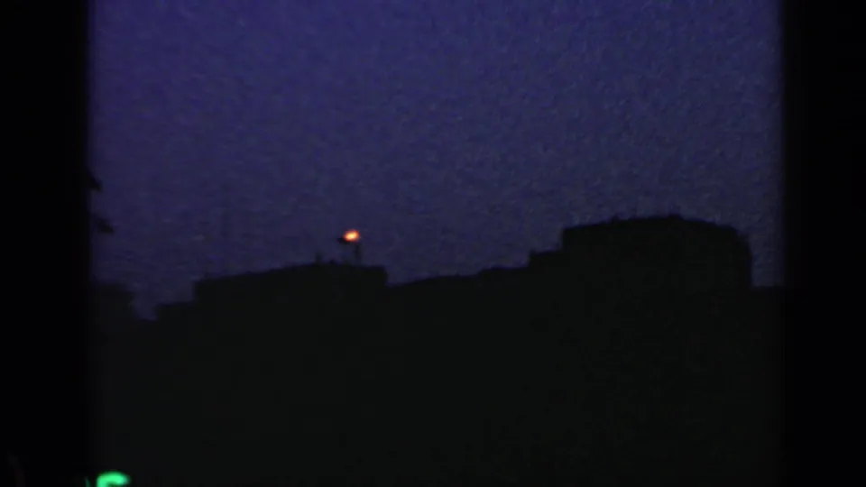Final 1960 Rome home-movie view showing a distant flame or light against dark waterfront silhouettes and blue evening sky.