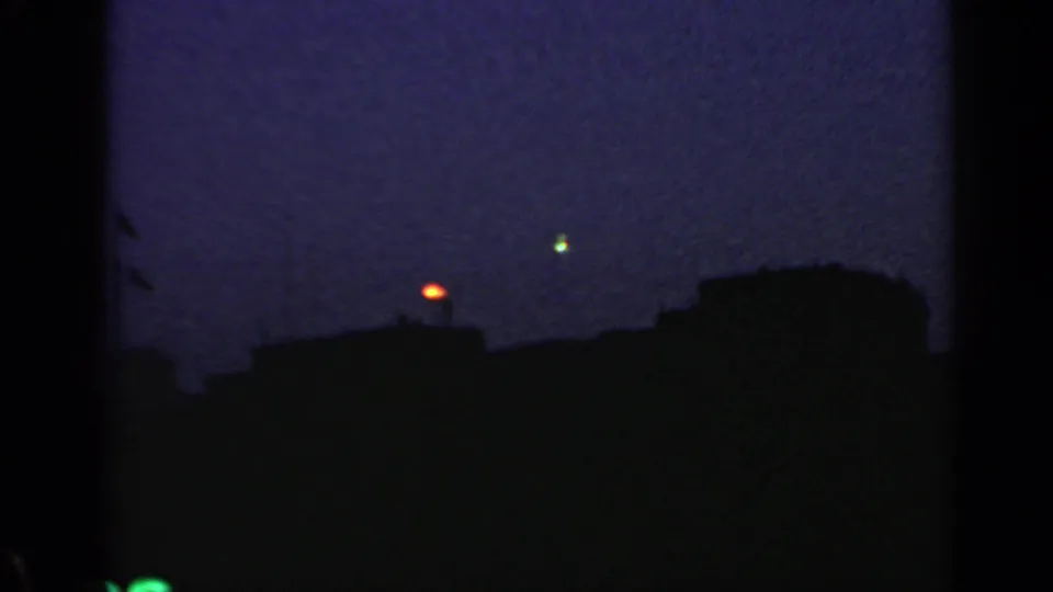 1960 Rome home-movie frame showing roof silhouettes, an orange light, and a brief green point in the sky.