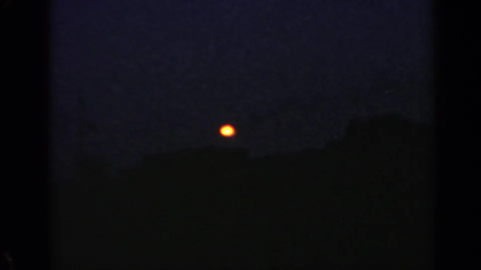 1960 Rome 8mm frame with a bright orange light above a nearly black rooftop silhouette at nightfall.