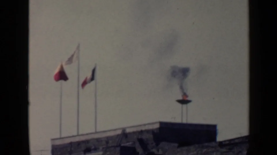 1960 Rome 8mm frame showing flags and a smoking brazier above a stone roofline, with soft focus and muted color.