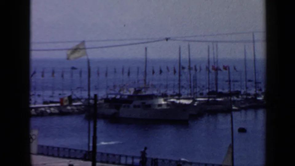 1960 Rome waterfront view with moored boats, many masts, strings of flags, railings, water, and a distant person.