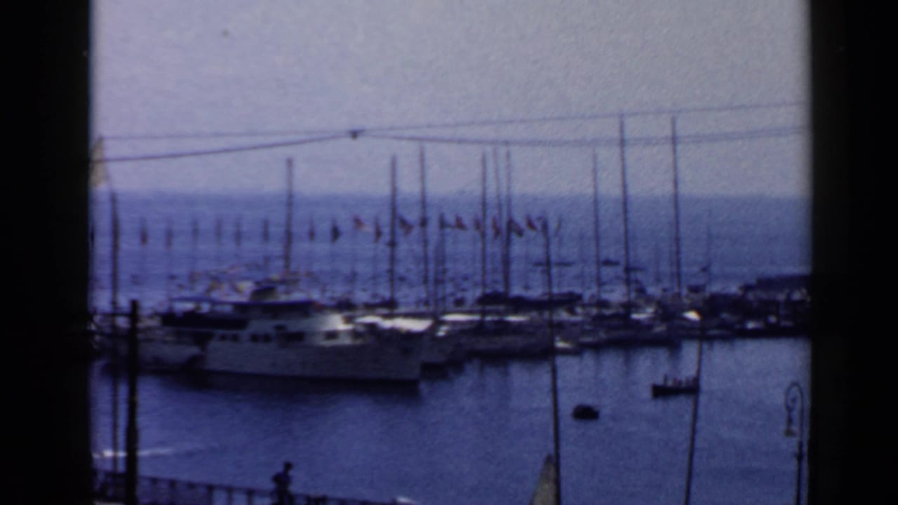 1960 Rome harbor view with a white yacht, clustered masts, flags along the dock, and dark vertical window framing.