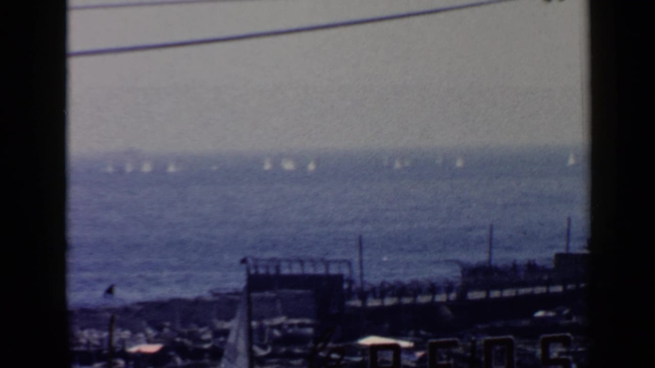 Distant sailboats on a blue sea beyond a dark waterfront and overhead wires.
