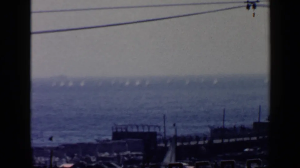1960 Rome seaside frame showing a hazy offshore view, small sailboats, a dark waterfront structure, and visible Super 8 frame borders.