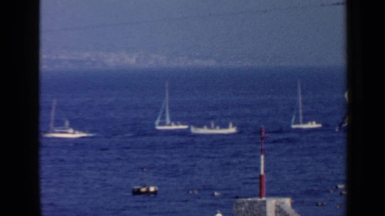 Sailboats and motorboats on blue water with a red-and-white pole in the foreground.
