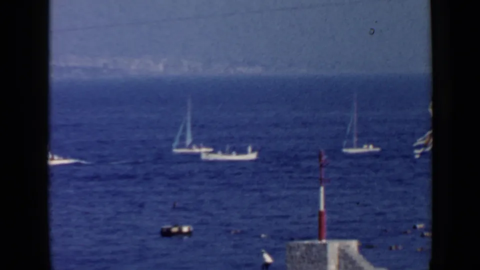 1960 Rome 8mm seascape showing boats offshore, a hazy horizon, dark framing, and a red-and-white pole near the lower edge.