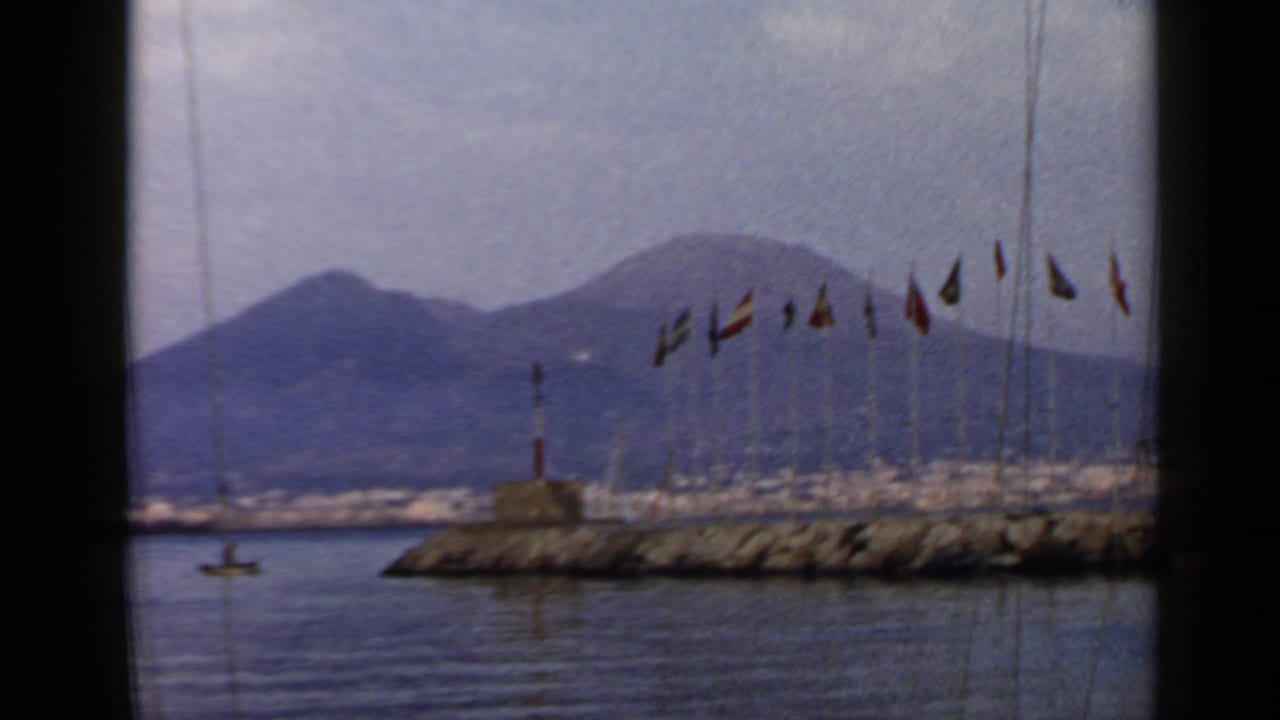 Harbor water, flagpoles, a breakwater lighthouse, and a distant volcanic mountain seen through dark framing.