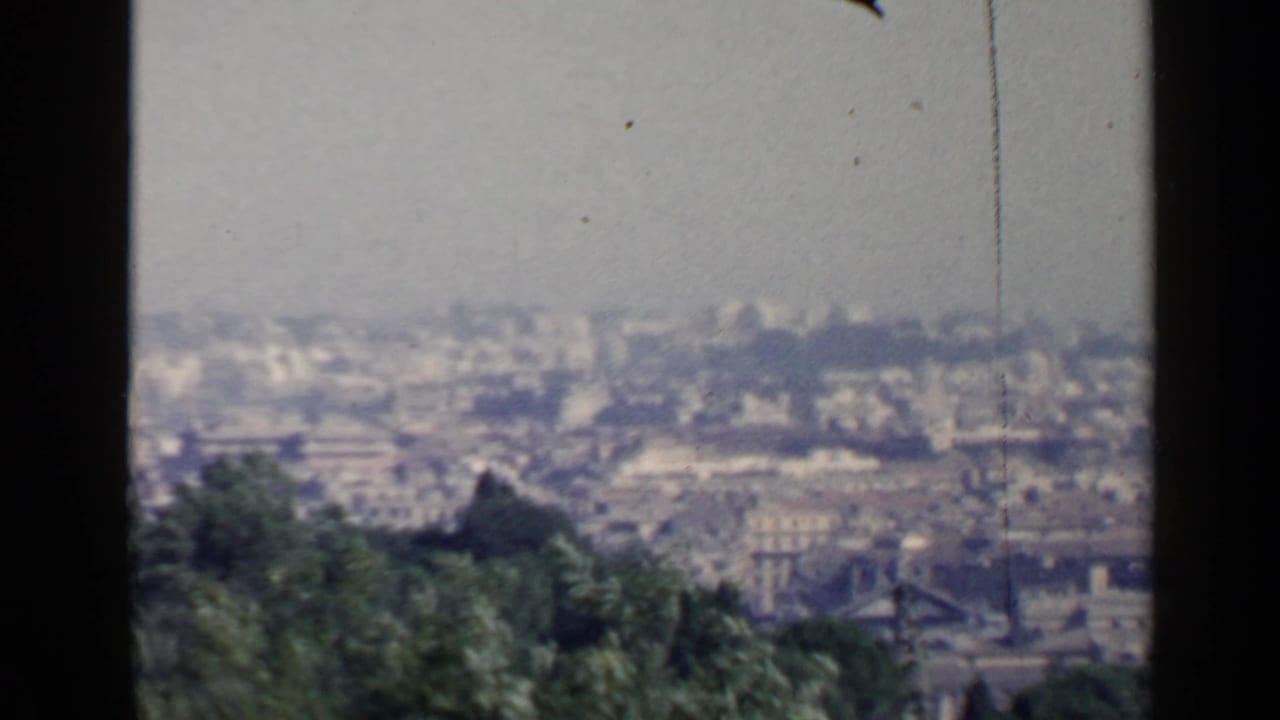 Hazy elevated view over Rome rooftops with trees in the foreground.