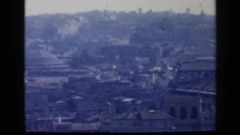 A soft 1960 8mm frame shows Rome's dense rooftops and distant hills, with arched architectural details near the lower right.