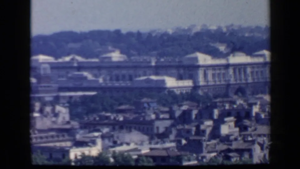 Rome cityscape from an elevated 1960 8mm home-movie view, with rooftops, a large facade, trees, and visible film frame edges.