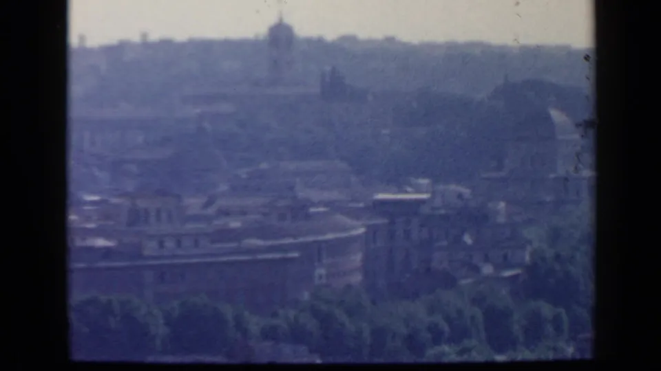 1960 Rome 8mm frame looking across treetops and urban roofs toward a hazy ridge with distant domed or tower forms.
