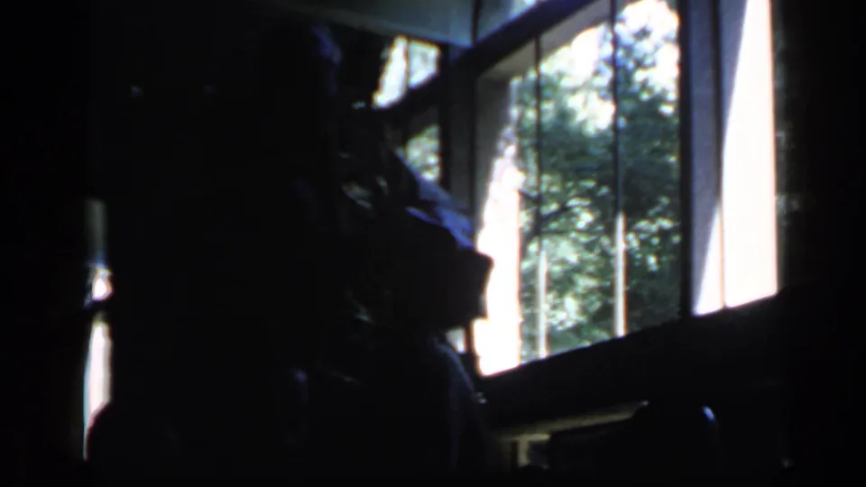 1960 Rome home-movie frame from inside a dark hall, with spectators silhouetted against tall windows and greenery outside.