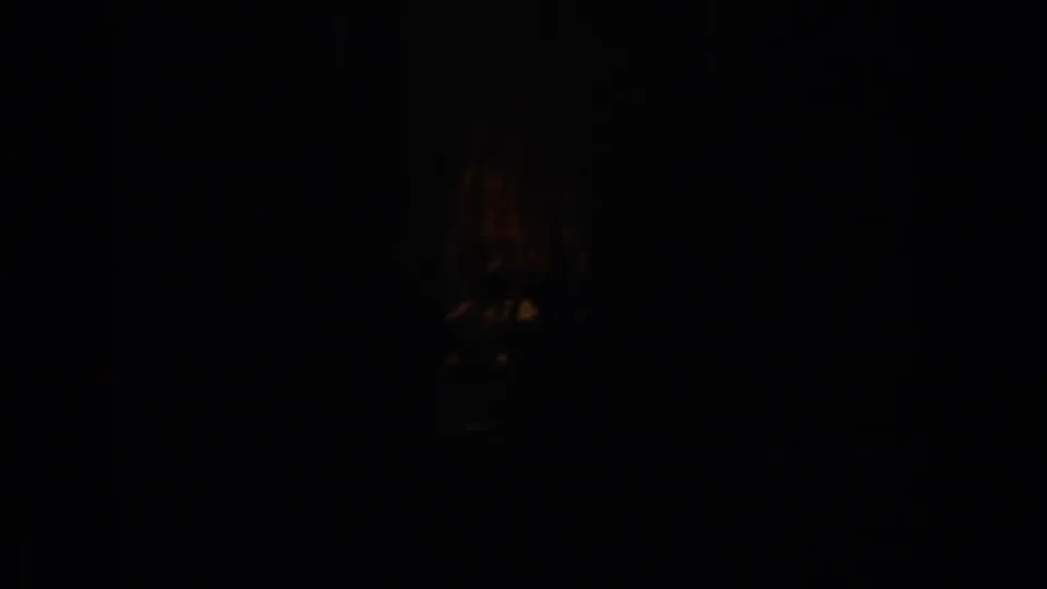 Very underexposed interior frame with only a faint warm-lit form visible in the darkness.