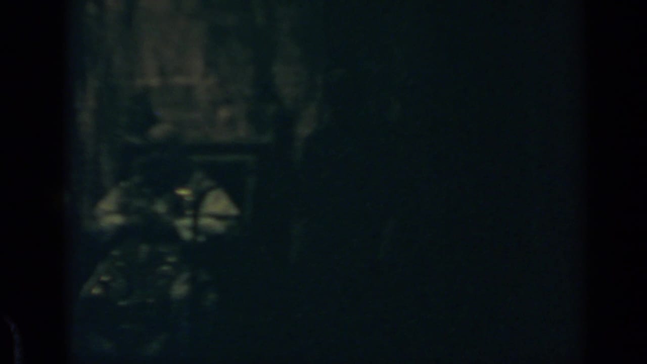 Dark, blurry interior with an indistinct figure or object near the lower left.