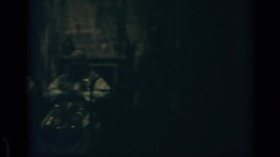 1960 Rome 8mm frame showing a dark interior, pale blurred shapes, and a possible person or object near the lower left.