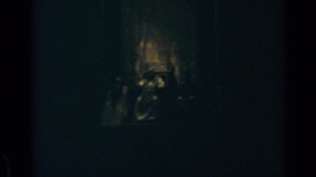 Very dark frame with a faint illuminated altar-like area and vertical film edges.