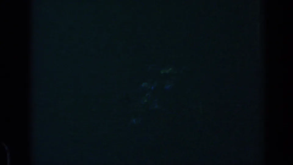 Near-dark 8mm frame from the Rome 1960 clip, with only faint silhouettes and heavy blue underexposure visible.