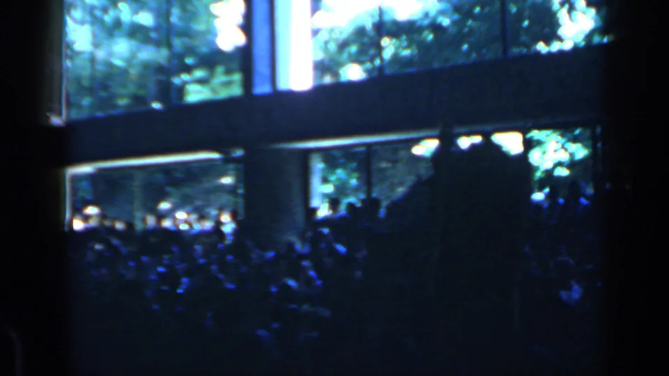 Rome 1960 home-movie frame with a crowded evening audience beside a lit window or venue facade.