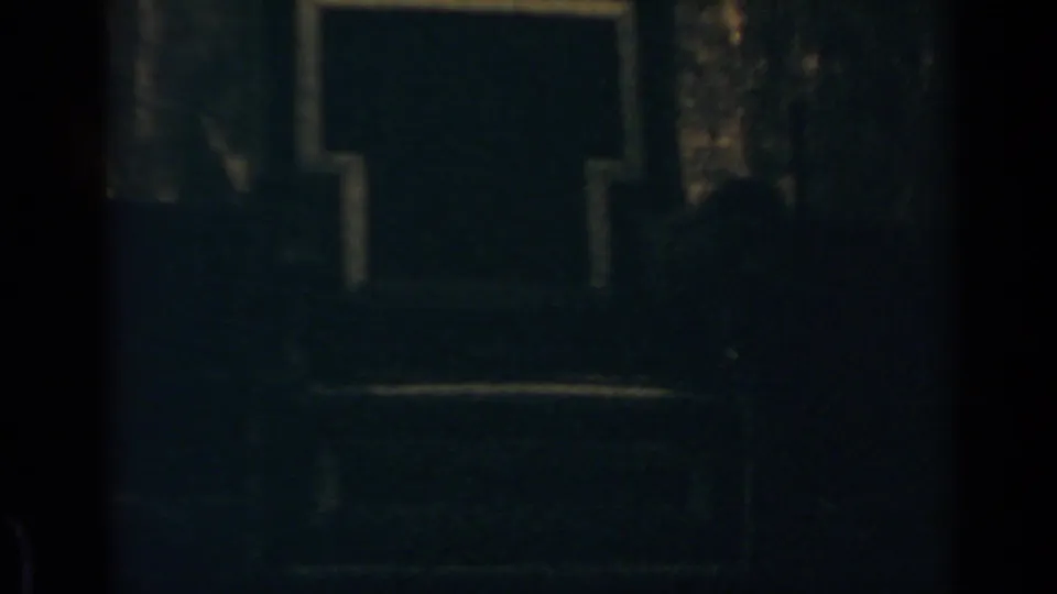 Dim 8mm frame from the Rome clip showing a shadowed facade and faint crowd forms near the lower edge.